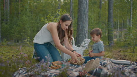 family-picnic-in-forest-young-mother-and-her-little-boy-are-sitting-on-blanket-and-preparing-food-weekend-at-nature